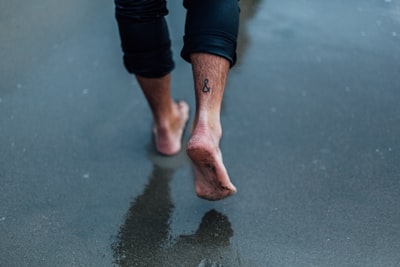 有纹身的人步行走在潮湿的沙滩

